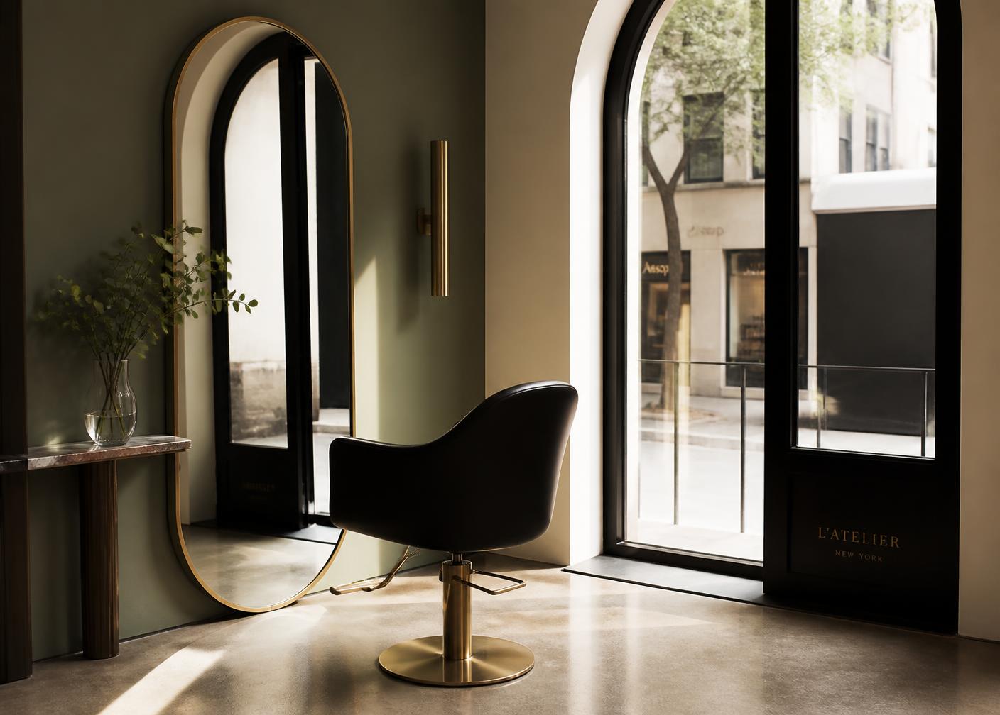 Sculptural styling chair beside an arched window in a sage green salon
